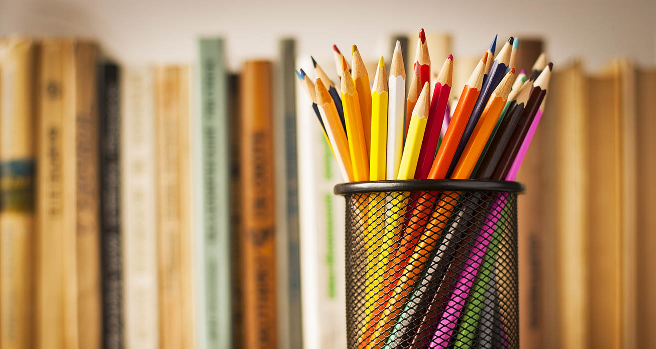 A container of coloured pencils sits on a desk