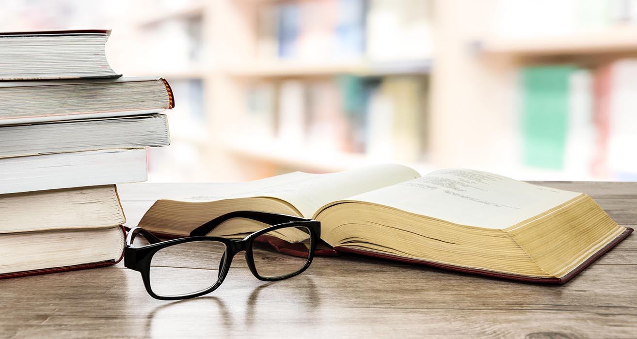 A stack of books and a pair of glasses sit on a desk